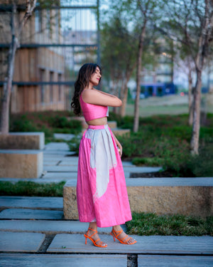Model wearing blush pink and ivory printed raw silk midi skirt, styled with a crop top in an urban garden setting
