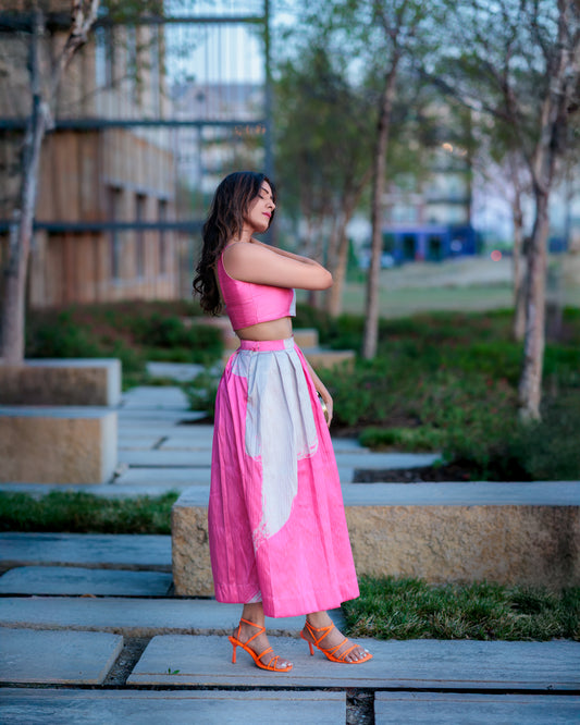 Model wearing blush pink and ivory printed raw silk midi skirt, styled with a crop top in an urban garden setting