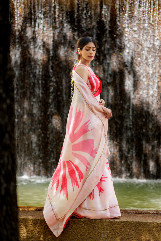Woman in a blush pink and white satin saree standing in front of a waterfall