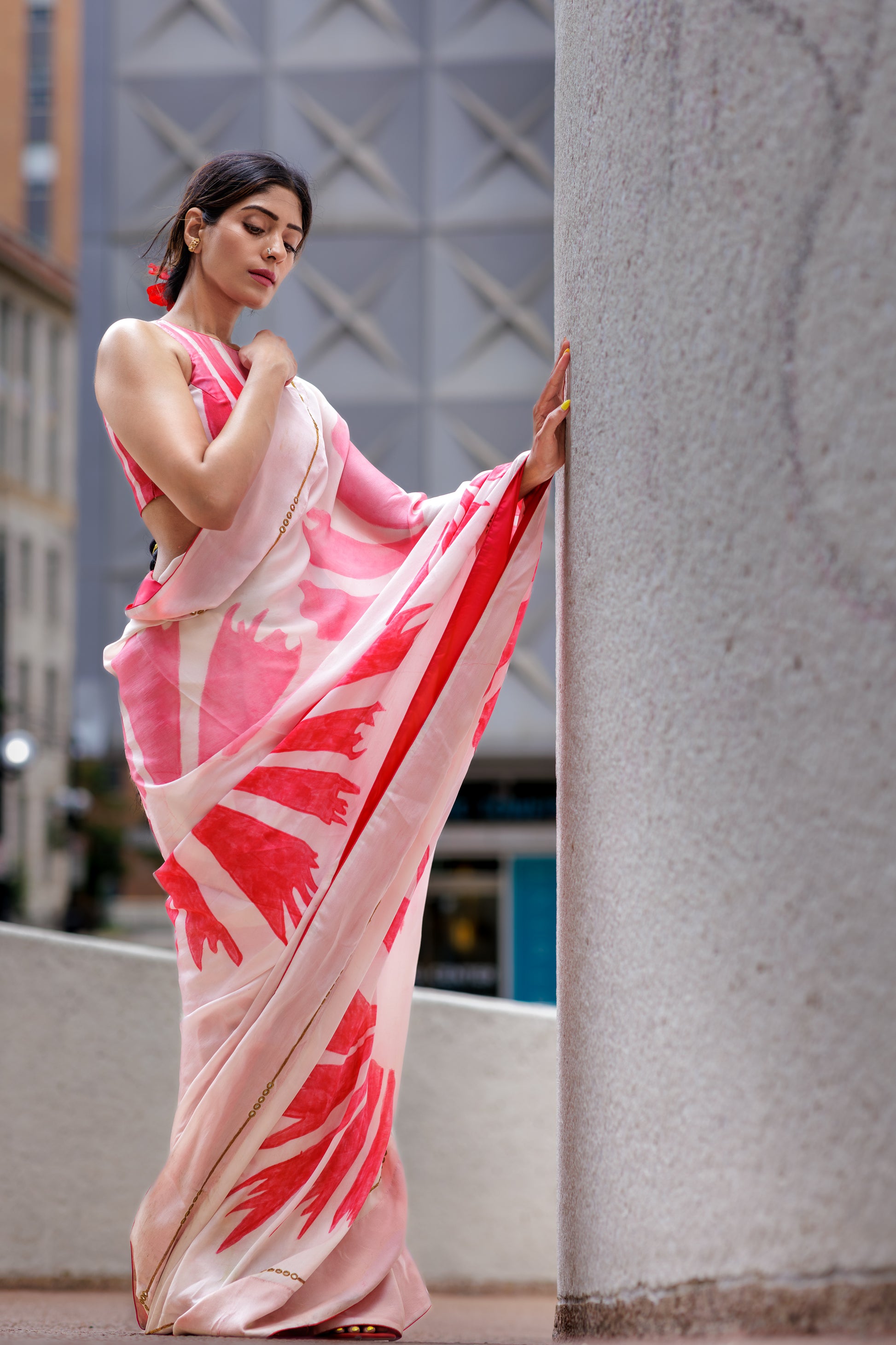 Woman in a pink and red saree standing against a building wall.