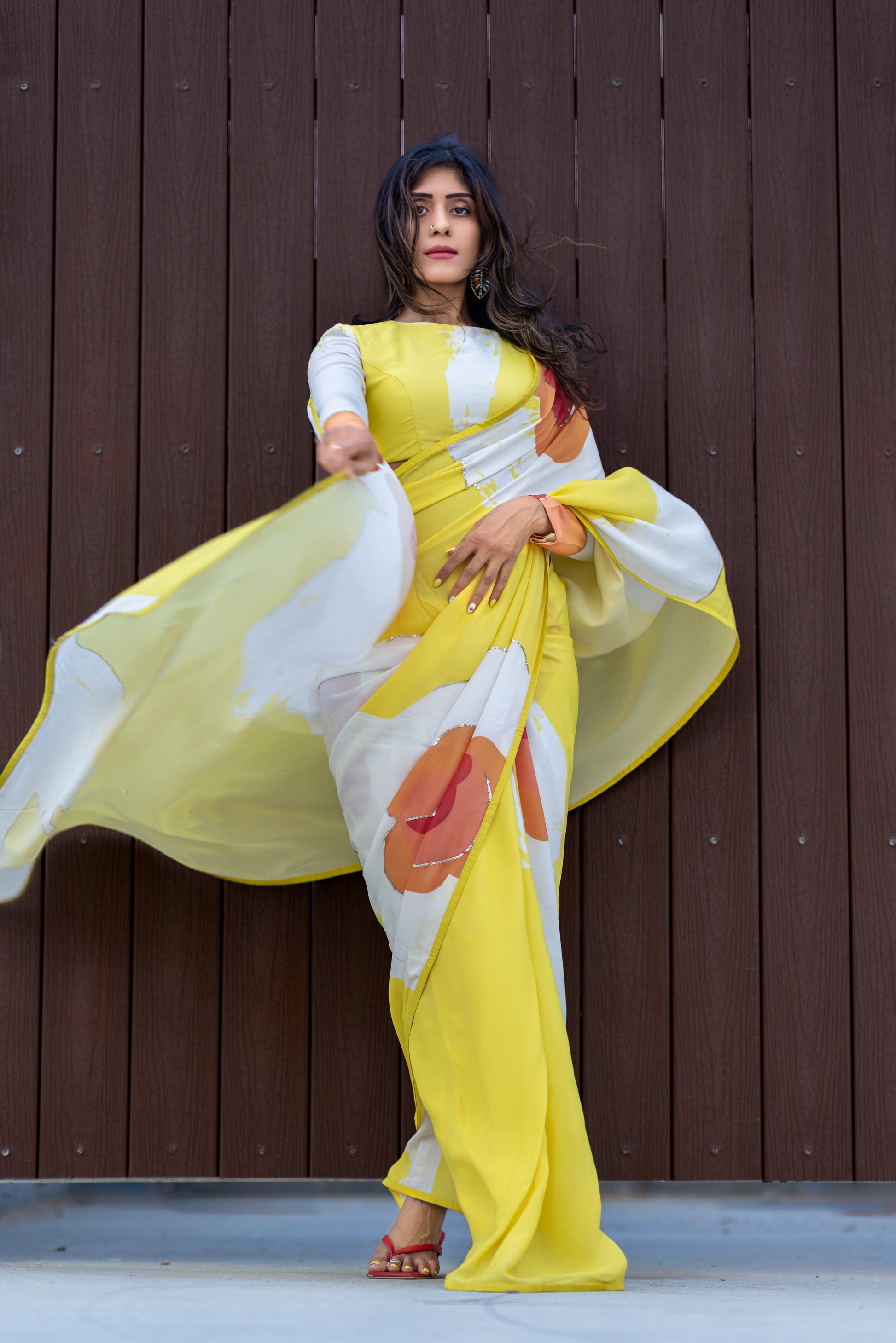 Woman in a yellow and white saree with floral patterns against a wooden background