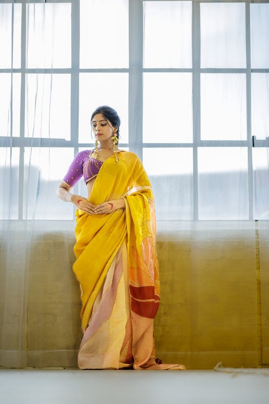 A woman wearing a yellow and orange hand painted pen kalamkari saree with a purple blouse hand embroidered with sequin and mirror work