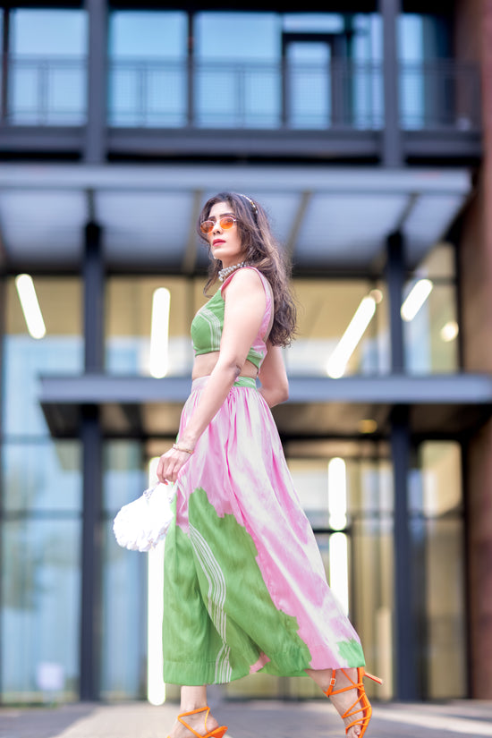 Wild petal raw silk abstract midi skirt in pink and green, styled with matching blouse, walking in front of modern architecture