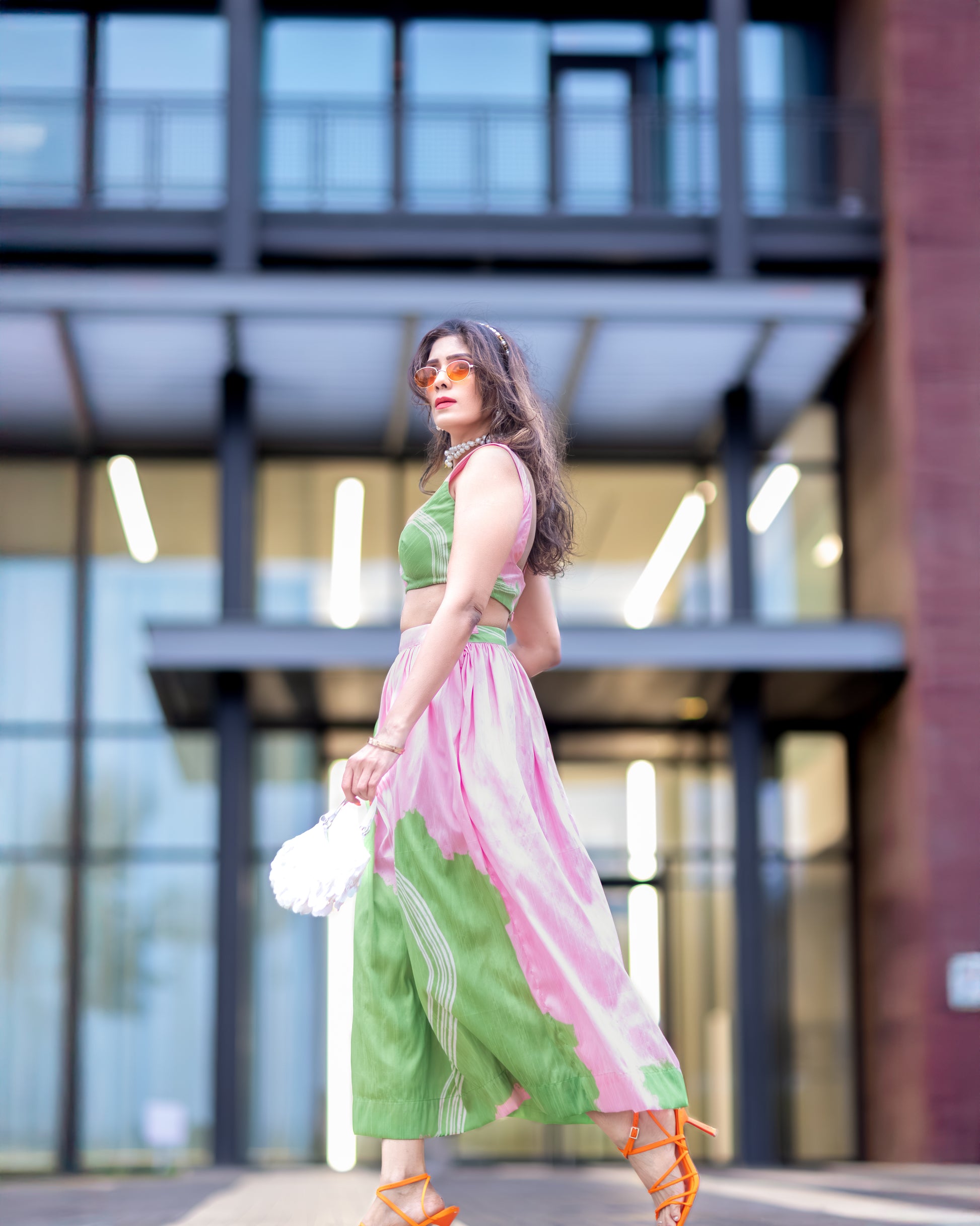Wild petal raw silk abstract midi skirt in pink and green, styled with matching blouse, walking in front of modern architecture