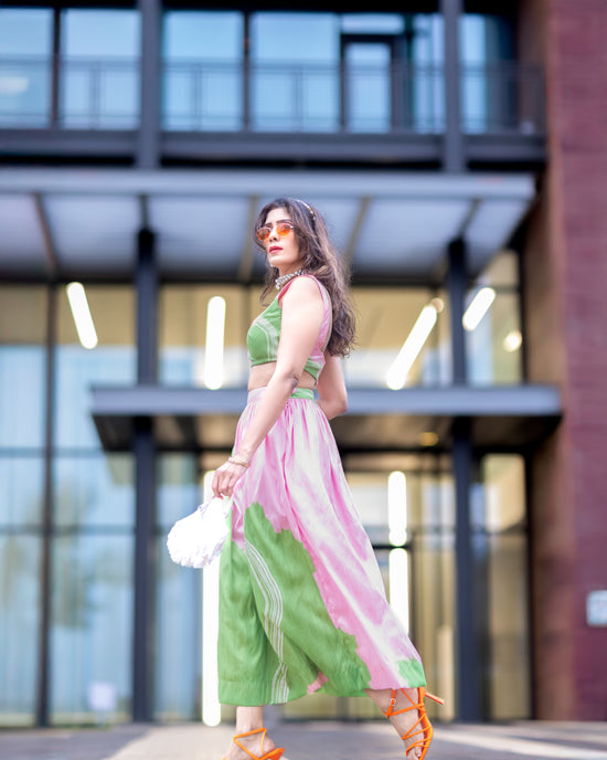 Wild petal raw silk abstract midi skirt in pink and green, styled with matching blouse, walking in front of modern architecture